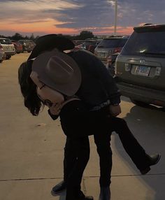 a man is kissing a woman in a parking lot at sunset with cars behind him