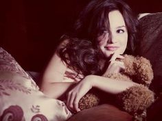 a woman laying in bed holding a teddy bear and smiling at the camera with her hand on her chin