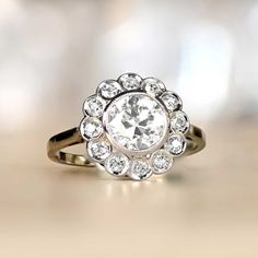 This Art Deco diamond cluster engagement ring centers an old European cut diamond weighing approx. 1.37ct, K color and VS1 clarity. The bezel-set center diamond is surrounded by a halo of antique single cut diamonds in a floral design. This vintage ring was handcrafted in 18k white gold in France, circa 1935. ✦DIAMOND SPECIFICATIONS: Center Diamond Weight: 1.37 Carats Diamond Color: K Color Diamond Clarity: VS1 Clarity Diamond Cut: Old European Cut ✦ ENGAGEMENT RING SPECIFICATIONS: Material: Pla Heirloom Moissanite Cluster Ring For Anniversary, Heirloom Style Moissanite Cluster Ring For Anniversary, Antique Brilliant Cut Diamond White Cluster Ring, Vintage White Wedding Ring With Halo Setting, White Vintage Wedding Ring With Halo Setting, Moissanite Cluster Ring With Rose Cut Diamonds For Anniversary, Antique Brilliant Cut Diamond Cluster Ring, Antique Diamond Cluster Ring With Brilliant Cut, Vintage White Diamond Ring With Halo Setting