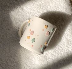 a white coffee cup sitting on top of a fluffy carpet next to a teddy bear