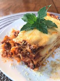 a piece of lasagna with meat and cheese on a white plate, garnished with a green leaf