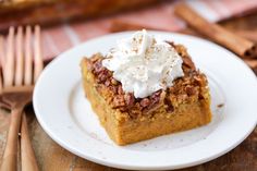 a white plate topped with a piece of cake covered in whipped cream and pecans