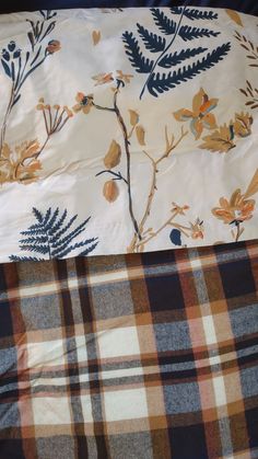 an unmade bed with plaid sheets and leaves on it