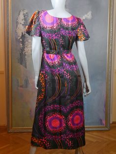 This 1970s mod dress has a stunningly vibrant purple, pink, and orange effervescent abstract polka dot pattern on a black satin sheen background. The dress has a round neckline and short sheer puff sleeves, and a fitted waistline with a matching belt gives way to an A-line drop to the midi-length hemline. The dress is lined in a black satin viscose-nylon fabric, and closes in the back with an 18.5-inch zipper. Bust = 40 inches (101cm) Shoulders = 16.5 inches (41.91cm) Waist = 32 inches (81.28cm) Multicolor Short Sleeve Evening Maxi Dress, Retro Multicolor Evening Dress, Retro Dresses With Vibrant Print For Party, Retro Party Dress With Vibrant Print, Fitted Retro Dress With Vibrant Print, Retro Purple Dress For Spring, Fitted Multicolor Retro Maxi Dress, Fitted Retro Multicolor Maxi Dress, Multicolor Short Sleeve Dress With Vintage Print