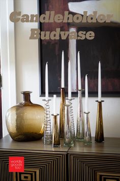 there are many vases and candles on the table next to each other in front of a painting