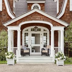 two chairs sitting on the front porch of a house with white pillars and windows,