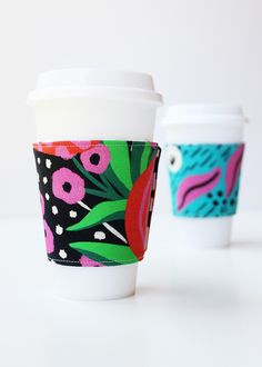 two coffee cups sitting next to each other on top of a white table with colorful designs