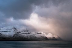 some snow covered mountains and water under a cloudy sky