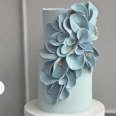 a blue and gold wedding cake with large flowers on the top, sitting on a white pedestal