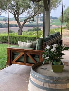 a porch swing with pillows and flowers on the back, in front of a tree