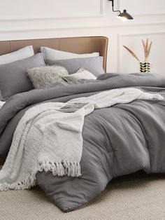 a bed with grey and white comforters in a small room next to a lamp