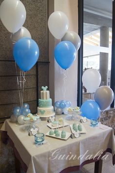 a table topped with blue and white balloons next to a cake on top of a table