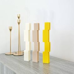 three candles are lined up on a table next to two vases and one candle holder