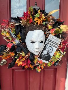 a white mask is hanging on a red door with autumn leaves and other decorations around it