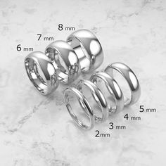 four different sizes of wedding rings on a marble surface with measurements for each ring size