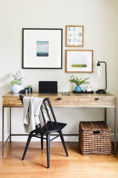 a wooden desk topped with a laptop computer next to a chair and pictures on the wall