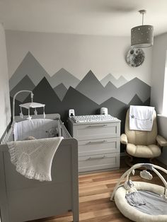 a baby's room decorated in grey and white with mountains painted on the wall