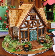 a house made out of gingerbread on top of a wooden table with other decorations