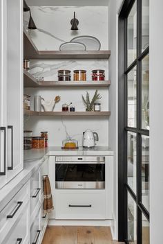 a kitchen with white cabinets and open shelvings on the wall, along with wooden flooring