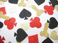 several hearts and spades are scattered on a white surface with gold, black, and red confetti