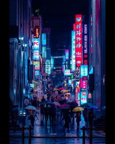 many people with umbrellas are walking down the street in the city at night time