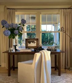 a white chair sitting in front of a window next to a table with flowers on it