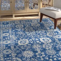 a blue and white area rug with an ornate design on the bottom, in front of a wooden cabinet