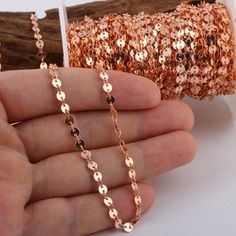 a hand holding a gold chain next to a roll of glittered paper and a piece of wood