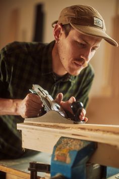 a man working on a piece of wood with a planer and visor in his hand