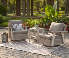 two chairs and a table on a brick patio with flowers in the backgroud