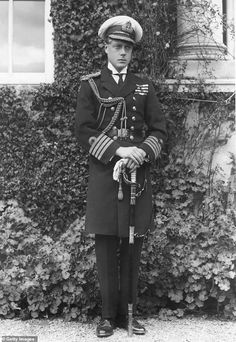 black and white photograph of a man in uniform standing next to a wall with ivy growing on it