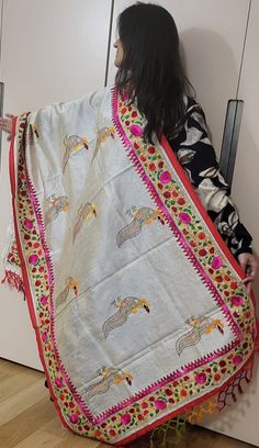 a woman holding up a white and red blanket with horses on it in front of a door