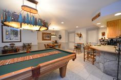 a pool table in the middle of a living room with an island and bar stools