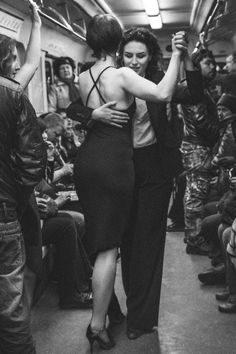 black and white photograph of two women dancing on a subway train with other people in the background