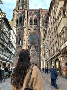 Eine Frau steht vor einer schönen Kathedrale, sie ist mit dem Rücken gedreht zum Fltografen. Sie hat lange braune Haare, einen beigen Manteln und eine Sonnenbrille auf dem Kopf an. A woman stands in front of a beautiful cathedral, with her back turned to the photographer. She has long brown hair, a beige coat, and sunglasses on her head. The picture is very pretty and gives of a good vibe. Strasbourg Winter, Strasbourg France Winter, Strasbourg Photo Ideas, Prague Photo Ideas Instagram, Salzburg Instagram Spots, Strasbourg France Aesthetic, Germany Picture Ideas, Germany Instagram Pictures, Germany Photo Ideas