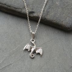 A Sterling silver flying dragon charm suspends from a sterling silver trace chain with lobster clasp fastening. The dragon charm measures 15 mm x 15 mm and is securely attached by a dainty sterling silver bail. There is a choice of 16 or 18 inch sterling silver chain. Dragons symbolize good luck. The necklace will arrive in a gift box. Would make a lovely gift for that special someone. Sterling Silver Necklace With Dragon Design, Sterling Silver Jewelry With Dragon Design Round Pendant, Silver Dragon Design Sterling Silver Necklace, Silver Sterling Necklace With Dragon Design, Silver Dragon Design Sterling Silver Jewelry, Sterling Silver Charm Necklace In White Gold, Gothic Pendant, Flying Dragon, Aventurine Necklace