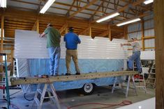 three men standing on top of a trailer in a warehouse with foam covering the floor