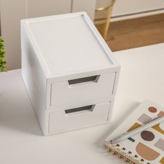 a small white box with two drawers next to a notepad and pen on a table