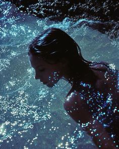 a woman is swimming in the water with blue lights on her body and back legs