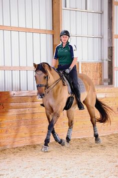 a woman riding on the back of a brown horse in an indoor arena with wooden walls