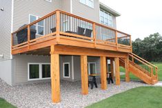 a house with a deck and stairs leading up to the second floor, next to a lawn