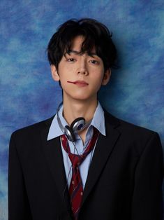 a young man wearing a suit and tie with headphones on his ears, standing in front of a blue backdrop