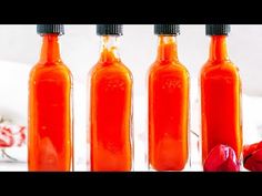 three bottles filled with orange liquid sitting on top of a white countertop next to red flowers