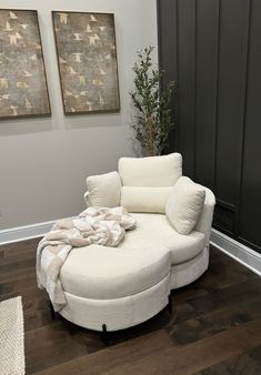 a white chair and ottoman in a room with wood flooring, two paintings on the wall