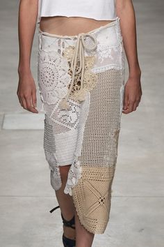 a woman walking down a runway wearing a skirt with crochet on the side