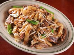 a white plate topped with noodles and meat on top of a wooden table next to a fork