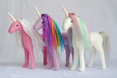 three stuffed unicorns standing next to each other on a white background with one pink, one blue and one green