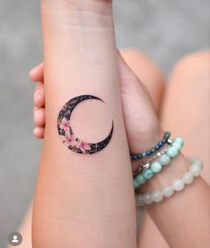 a woman's arm with a tattoo on it that has a crescent and flowers