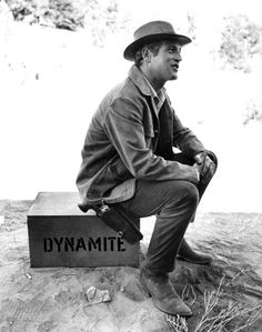 a man sitting on top of a box with dynamite written on the side in black and white