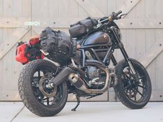 a black motorcycle parked in front of a garage door with luggage on the back tire